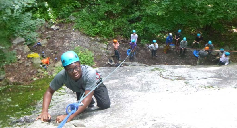 From above, you can see a rock climber wearing safety gear making their way up a rock wall